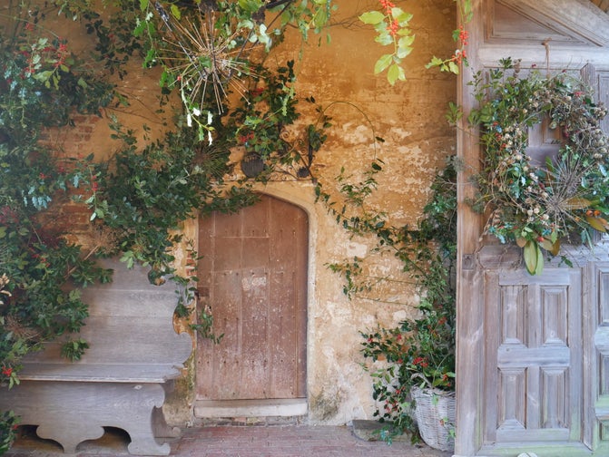 A collection of evergreen vines and branches in front of a beige wall and wooden door